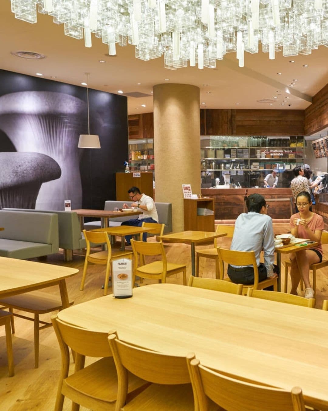 Café&Meal MUJI – Minimalist Study Space with Warm Interiors Elegant chandelier and uniform yellow seating at Café&Meal MUJI Singapore with people working